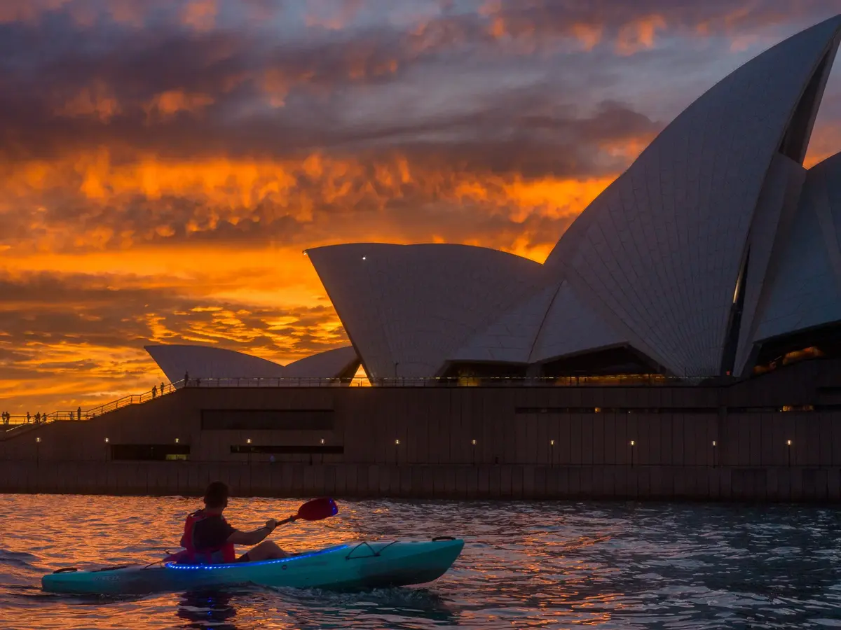 Kayaker paddling past Sydney Opera House during vivid orange sunrise on the water
